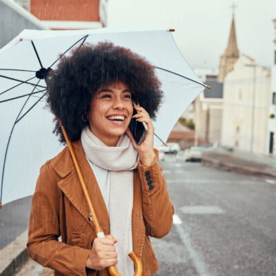 A young woman holding an umbrella while talking on the phone.