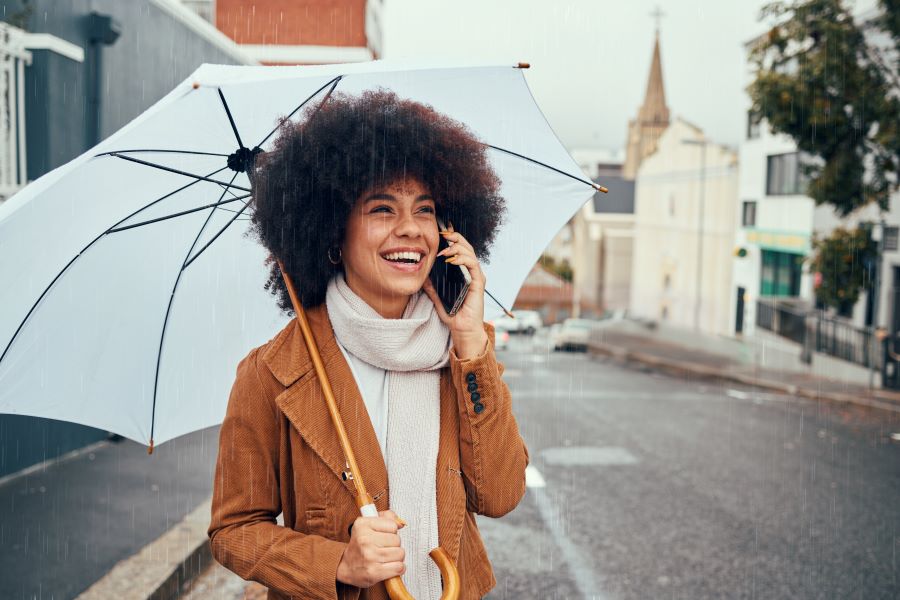 A young woman holding an umbrella while talking on the phone.