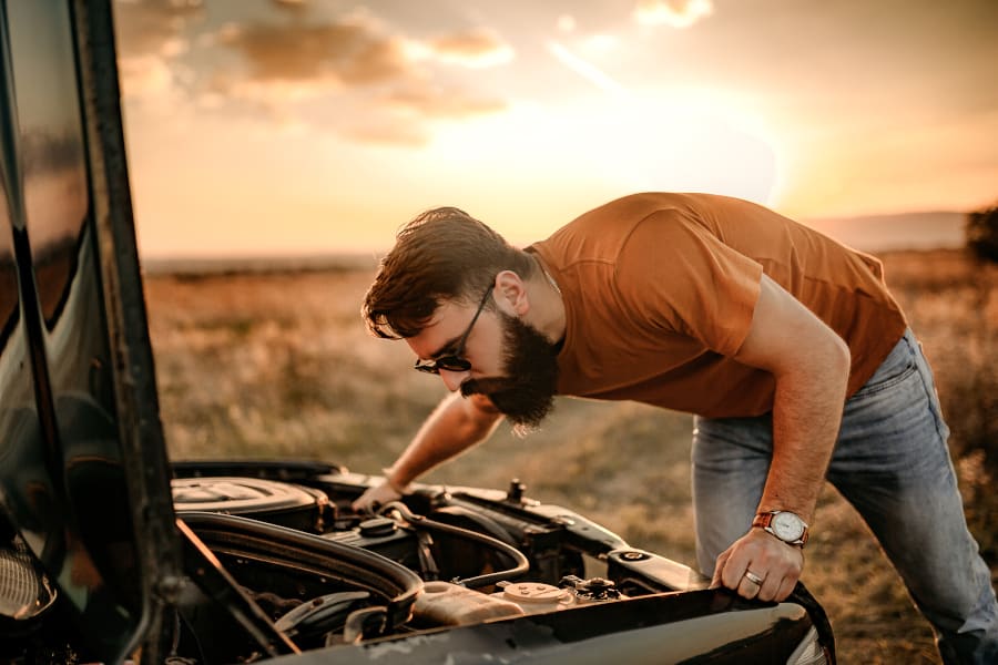 A man with a beard is looking at the engine of his car.