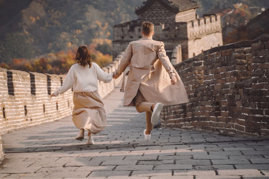 An adult and child holding hands, running happily away from the camera along an ancient defensive wall.