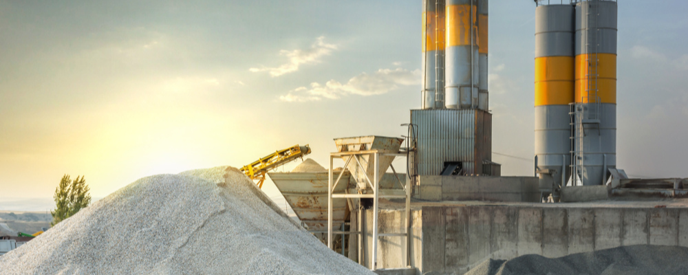 A cement quarry in the daytime, 2 grey and yellow chimneys rising above a pile of rocks and gravel.