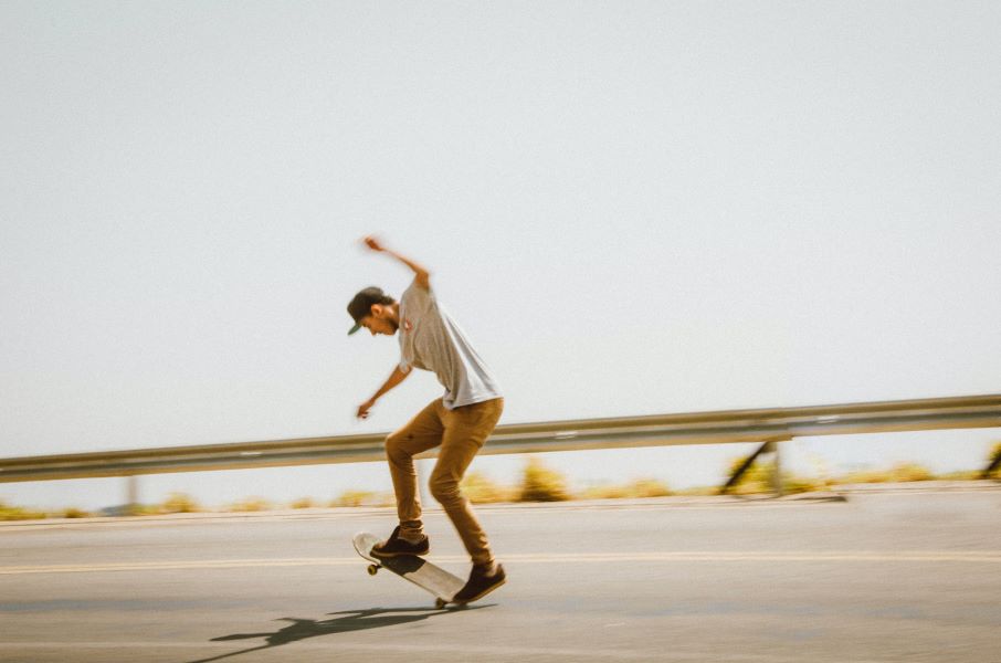 A skateboarder rolls along the road at high speed, his board balanced on the back wheels, the front wheels in the air.