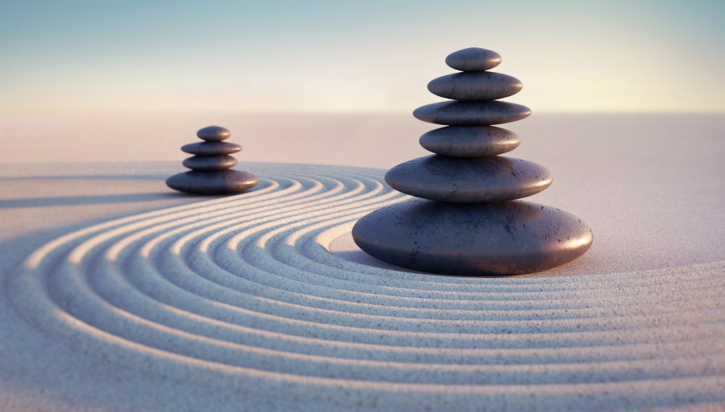 Two vertical stacks of smooth stones in soft white sand. A trail of rake marks winding through and between the two stacks.