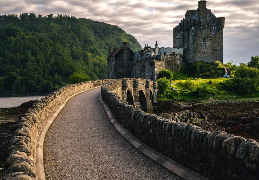 A path in a country setting winding it's way towards a castle, with a low stone wall on each side of the path.