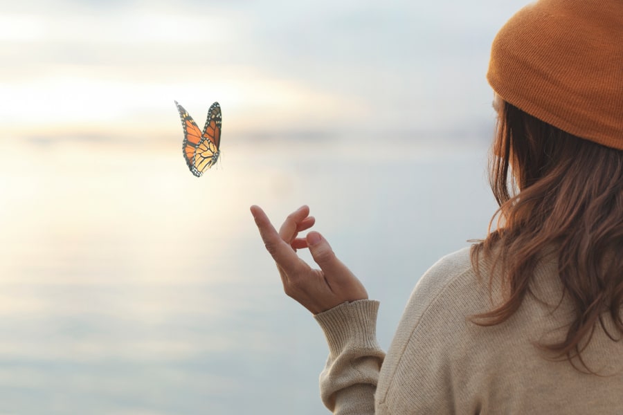 A butterfly flutters gently above a woman's hand as she looks at it.