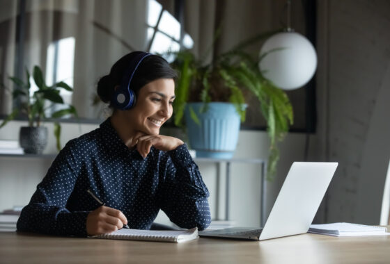 A woman wearing headphones and sitting at a desk with a laptop.