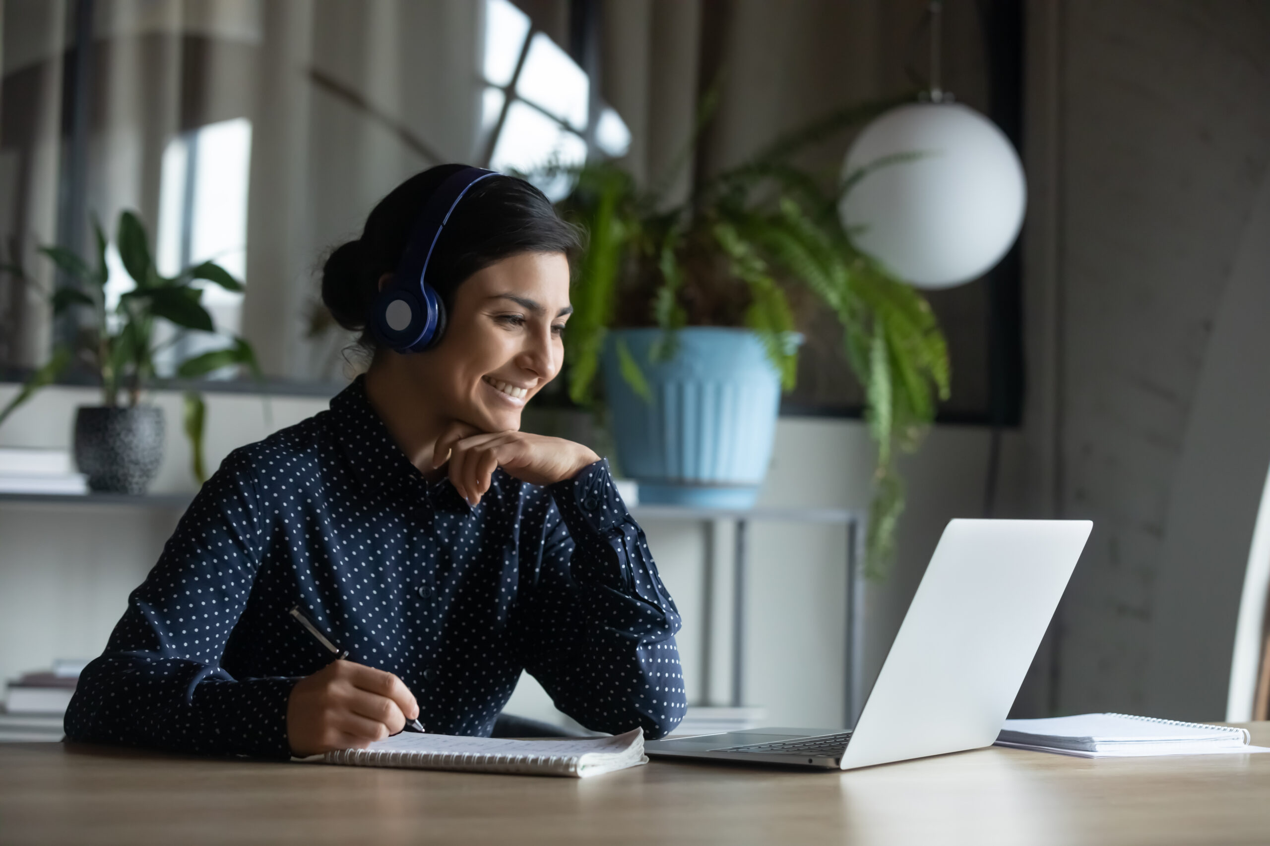 A woman wearing headphones and sitting at a desk with a laptop.