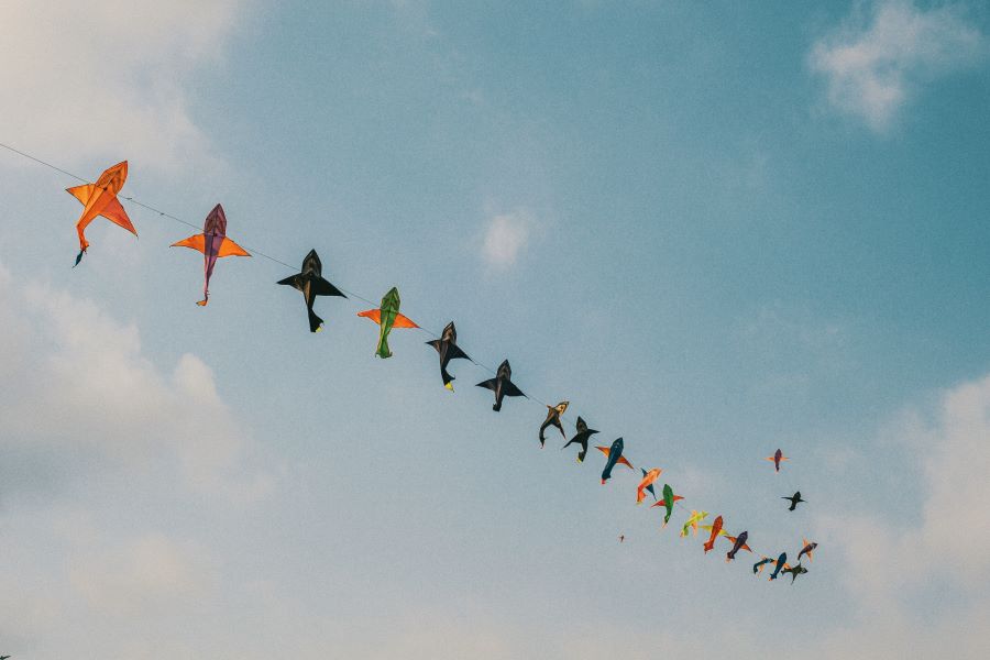 A trail of small kites all attached to a single line stretching away from us and up into the blue sky.