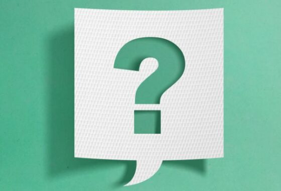 A square speech bubble made of white card, in front of a light green background. The shape of a question mark is cut out of the centre of the speech bubble,