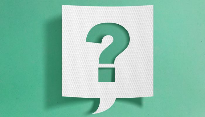 A square speech bubble made of white card, in front of a light green background. The shape of a question mark is cut out of the centre of the speech bubble,