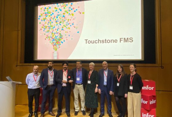 A group of people standing in front of a screen with the words Touchstone FMS.