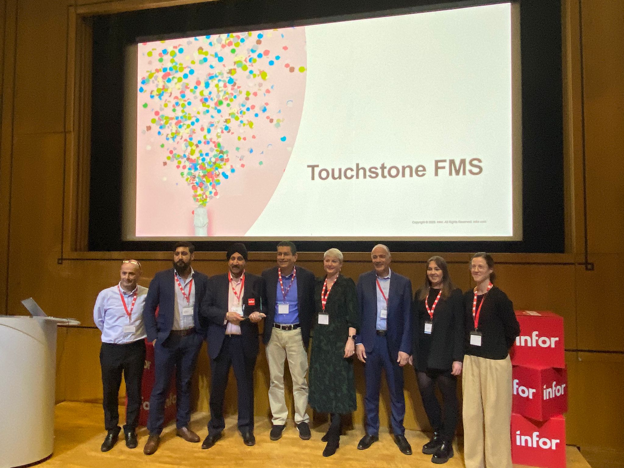 A group of people standing in front of a screen with the words Touchstone FMS.