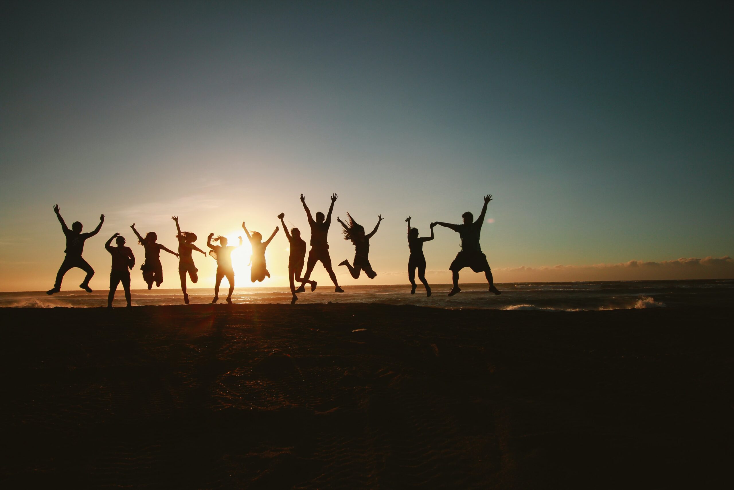 A group of people jumping on the beach at sunset.