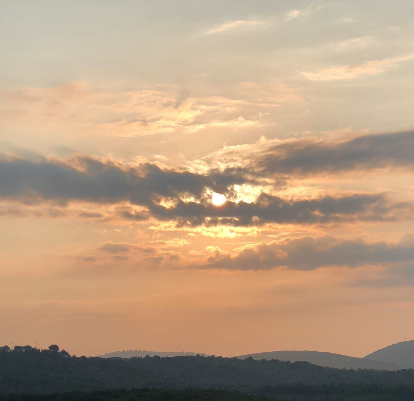 A sunset over a hill with trees and hills in the background.