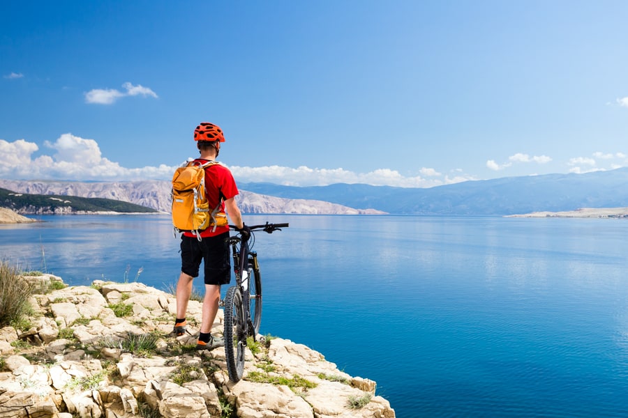 A mountain biker stands by their bike at a scenic spot, looking out over a bright blue lake.