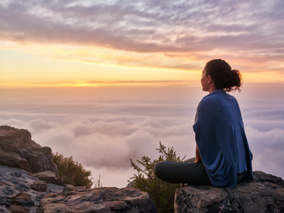 A woman is sitting on top of a mountain overlooking the clouds.