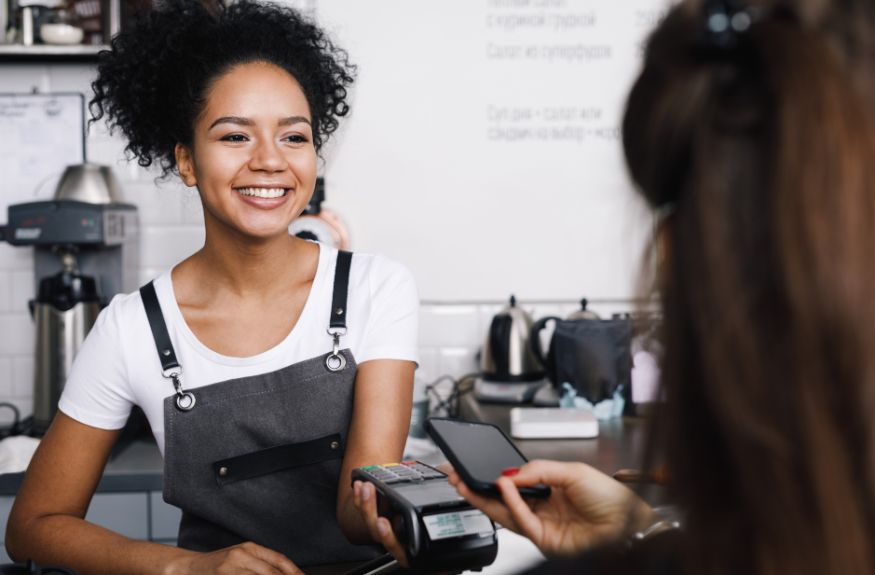 A woman in an apron is smiling at a customer in a coffee shop