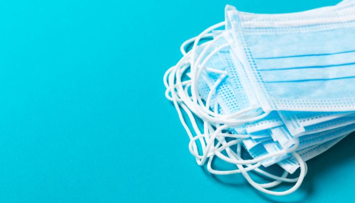 A stack of disposable face masks is seen from the centre to the right edge of this image, against a bright blue background.