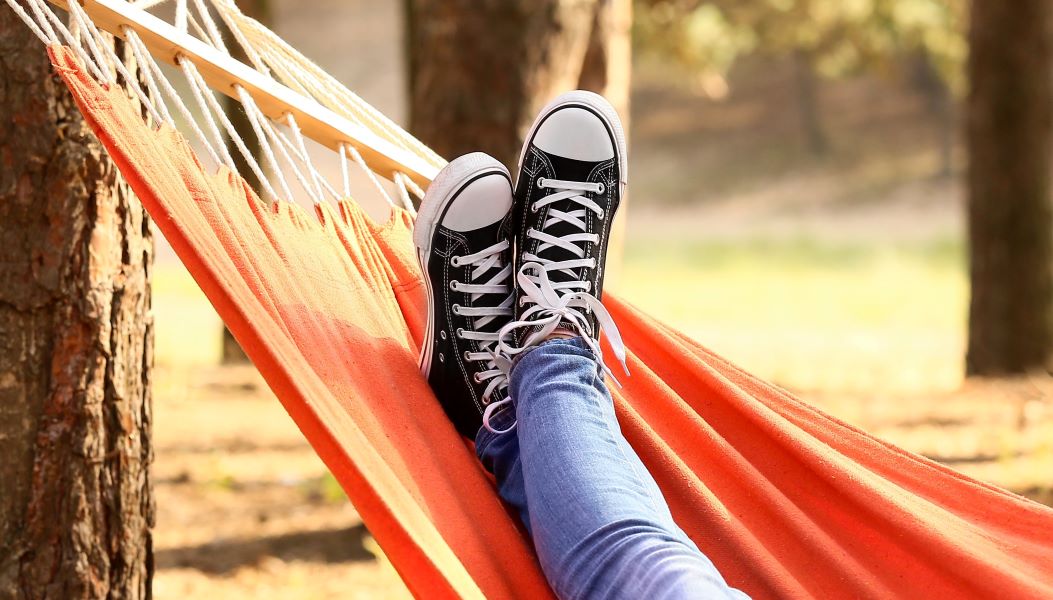 Two feet wearing trainers crossed in relaxation as their owner lies in a hammock.