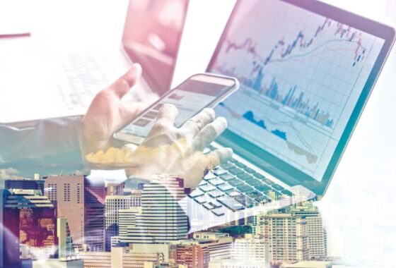 A person is using a laptop and a smart phone with a graph on it.