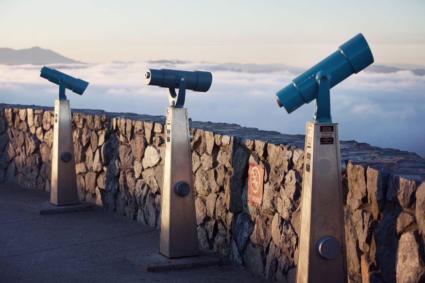 Three binoculars on a wall with clouds in the background.