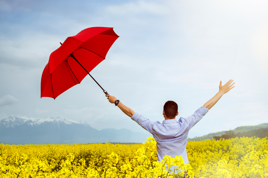 A man standing in a field with a red umbrella.