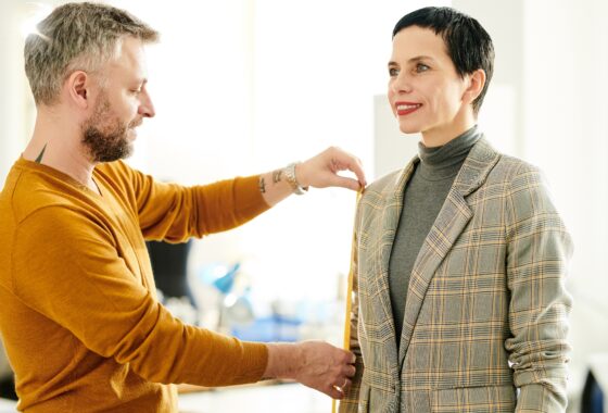 A man is measuring a woman's suit in an office.