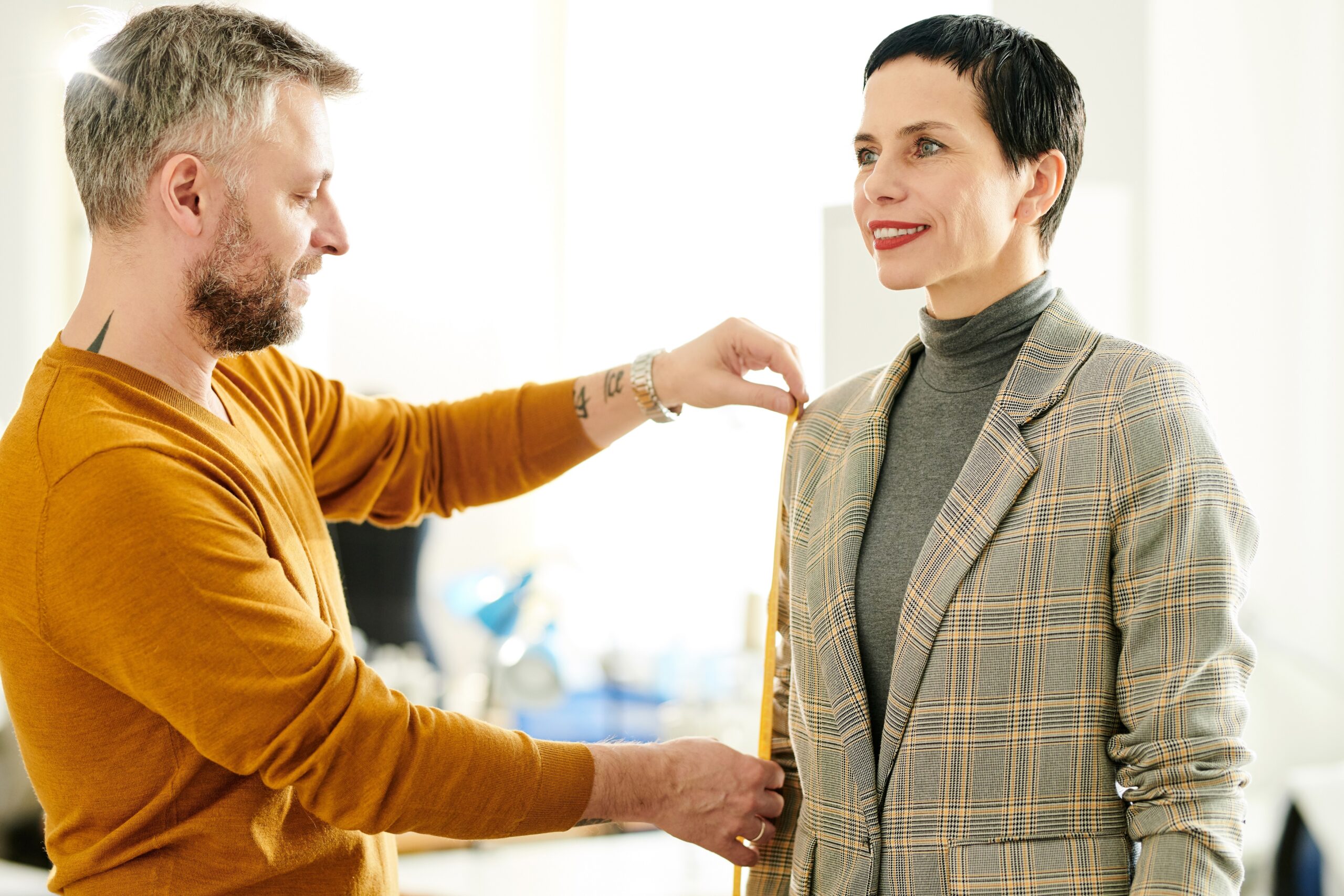 A man is measuring a woman's suit in an office.