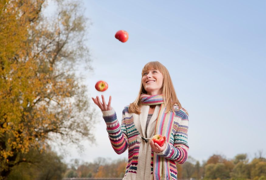 A young woman juggling apples in the park.