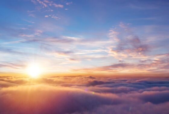 A bright, clear sky seen from above cloud level, the sun seen in the distance slightly to the left of shot.