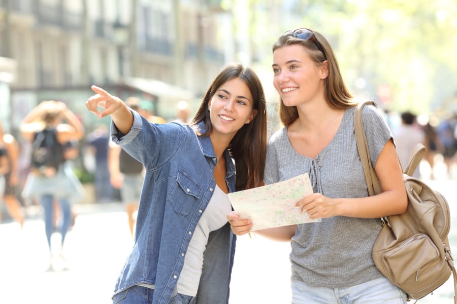 A woman giving another woman directions in a busy pedestrian area.