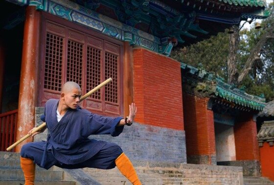 A chinese man practicing martial arts in front of a building.