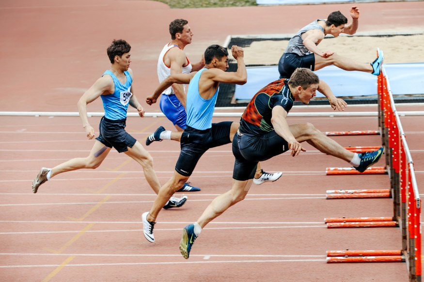 A group of men running over hurdles on a track.