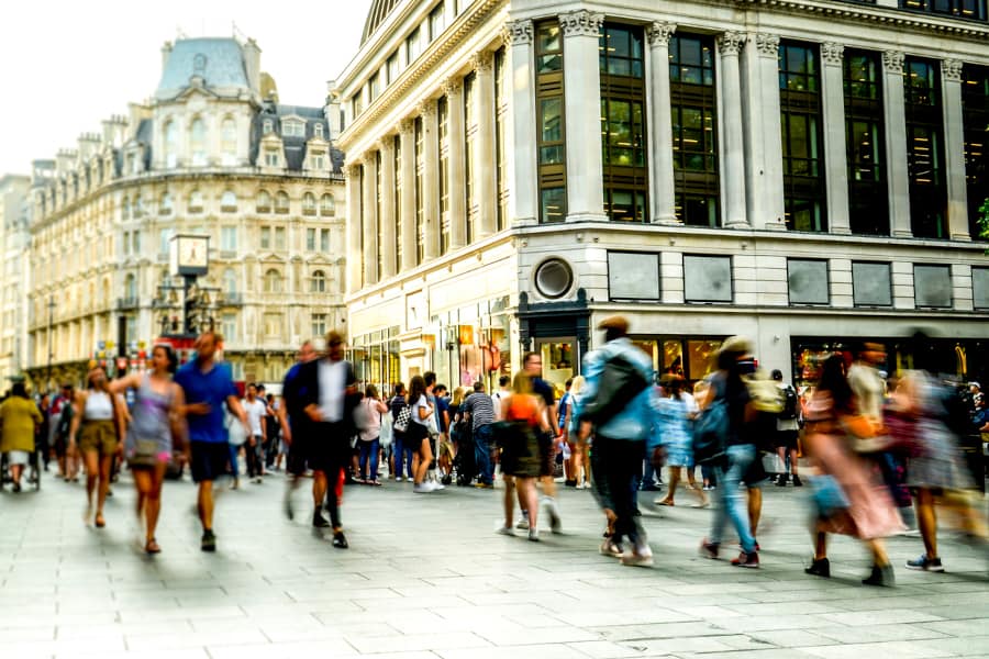 A busy pedestrian area in the daytime, people blurred slightly as they walk past the camera.