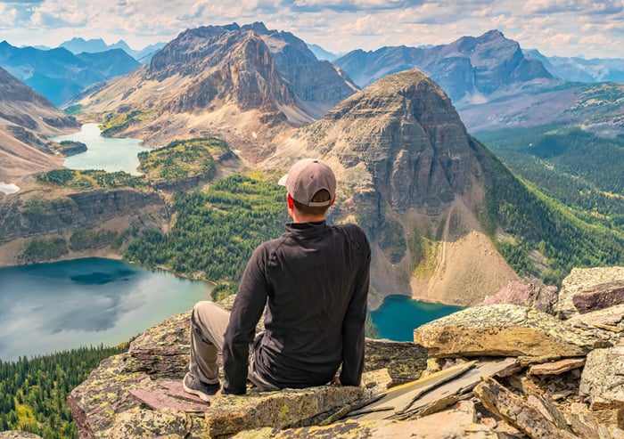 A man sits on top of a mountain overlooking a lake.