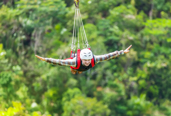 A man enjoying a zip-line, arms outstretched as if flying over the forest.