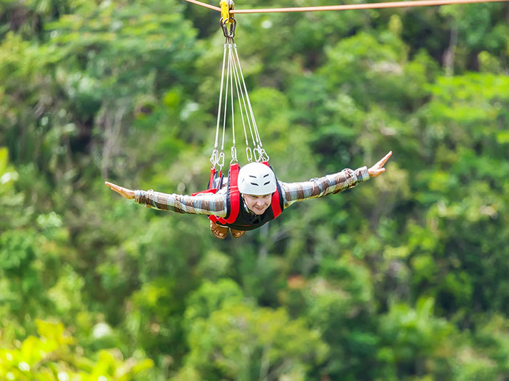 A man enjoying a zip-line, arms outstretched as if flying over the forest.