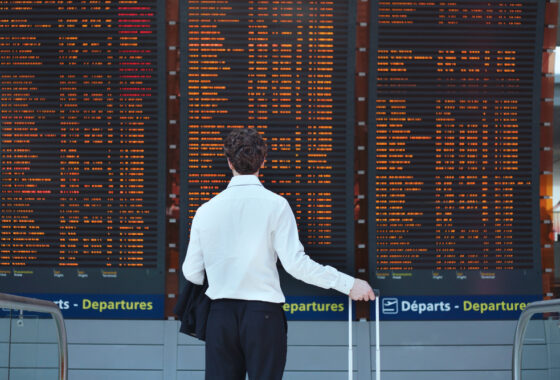 A man in a suit with a travel case looking at a large departures board.